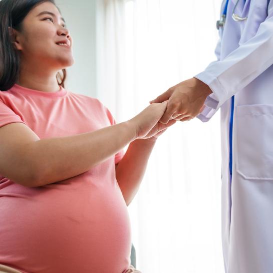 Smiling pregnant Asian woman talking to physician