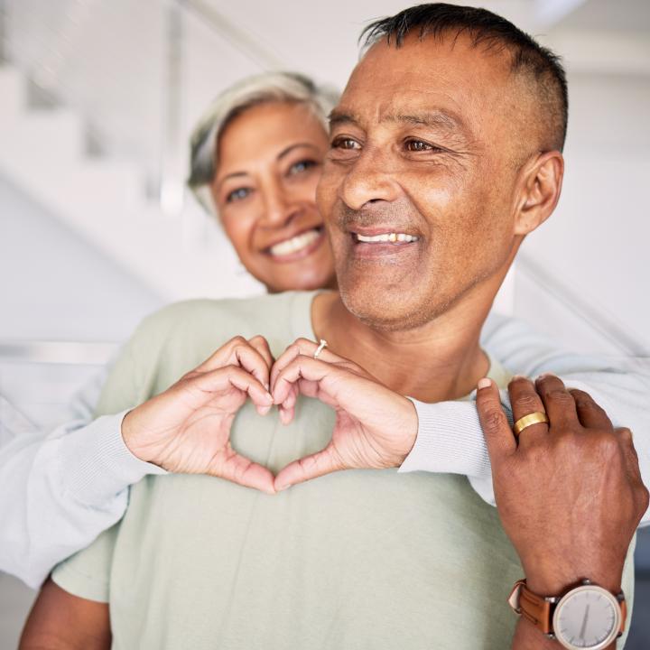 Smiling wife with arms wrapped around husband making heart sign with her hands