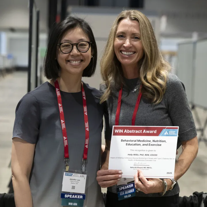 Two smiling women at a conference, one holding a white award certificate.