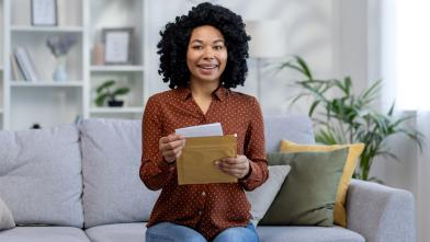 Smiling African American woman on couch opening a letter