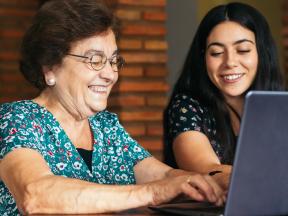 Smiling Latino grandmother and grand daughter looking at laptop computer