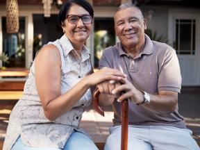 Smiling senior Latino couple clasping hands on top of walking cane