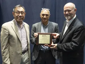 Photograph: Two men present an award plaque to a third man, all smiling.