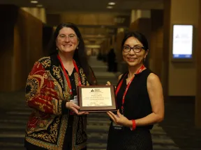 Two smiling women hold a framed certificate at an ADA event.