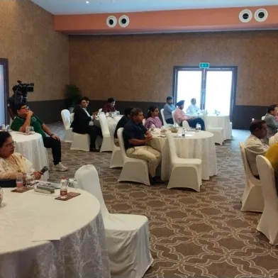 Photograph: Diverse group of attendees at an indoor conference, seated at white round tables.