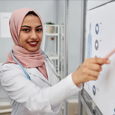 Smiling doctor in hijab and lab coat points to a medical chart.
