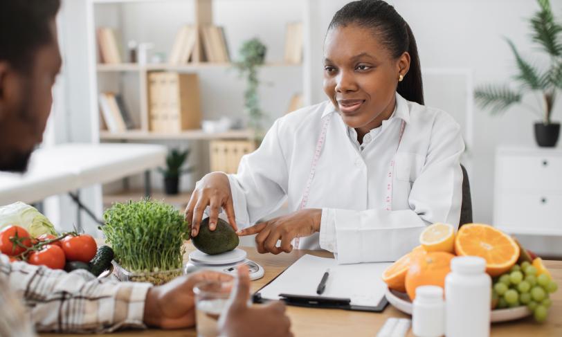 African American female nutritionist weighing avocado on scale