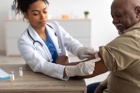 African American female physician putting bandage on senior African American male arm after vaccination