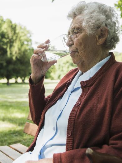 Senior woman sitting on park bench drinking a glass of water