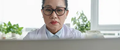 Woman doctor in lab coat and glasses, focused on laptop.