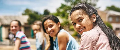Smiling girls look back at the camera outdoors, the front girl has braces.